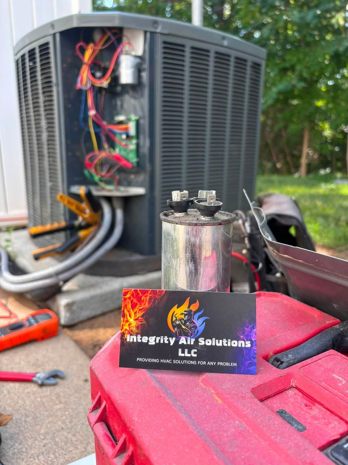 A failed capacitor pulled from a condenser, with an Integrity Air Solutions business card